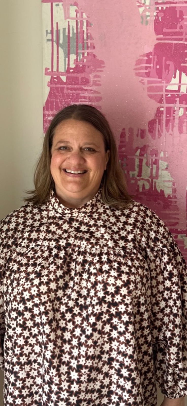 Portrait of Prudence Milligan, founder of Shoes & Booze, wearing a star-patterned blouse in front of pink abstract art.